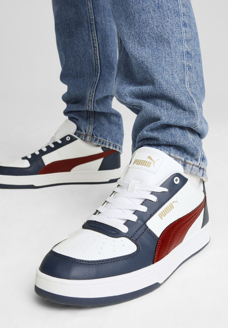 Las zapatillas Puma cuentan con una parte superior de cuero blanco con acentos en azul marino y rojo, una puntera perforada, cordones planos y una suela de goma texturizada.
