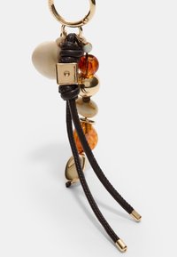 Accessoire de porte-clés avec quincaillerie en métal doré, cuir tressé marron et divers perles décoratives dans des teintes crème, ambre et or.