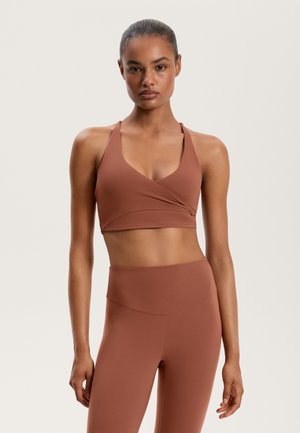 Sportowy stanik Brandy oraz legginsy w stonowanej brązowej kolorystyce. Stanik ma design w stylu wrap z halterowymi ramiączkami, bezszwową teksturę oraz legginsy o wysokim stanie.