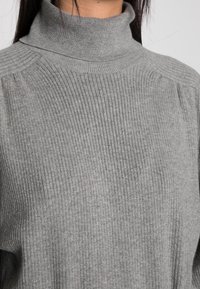 Helles graues geripptes Rollkragensweater mit taillierter Passform, das über eine erhöhte Textur und subtile Schulterdetails verfügt. Weiches Strickmaterial.