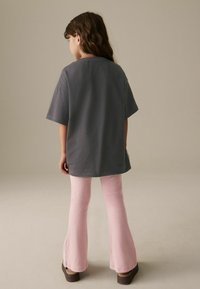 T-shirt gris surdimensionné associé à des leggings roses évasés. Le tissu semble doux avec une texture subtile, porté avec des sandales compensées marron.