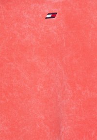 T-shirt en coton corail avec une finition douce et texturée. Présente un petit logo brodé bleu marine, blanc et rouge sur le côté gauche.