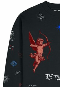 Sweat-shirt noir avec un chérubin rouge tenant un arc et une flèche, texte blanc « KISS HERE », « JE T’AIME », « AMOR », et divers petits symboles sur la manche et la poitrine.