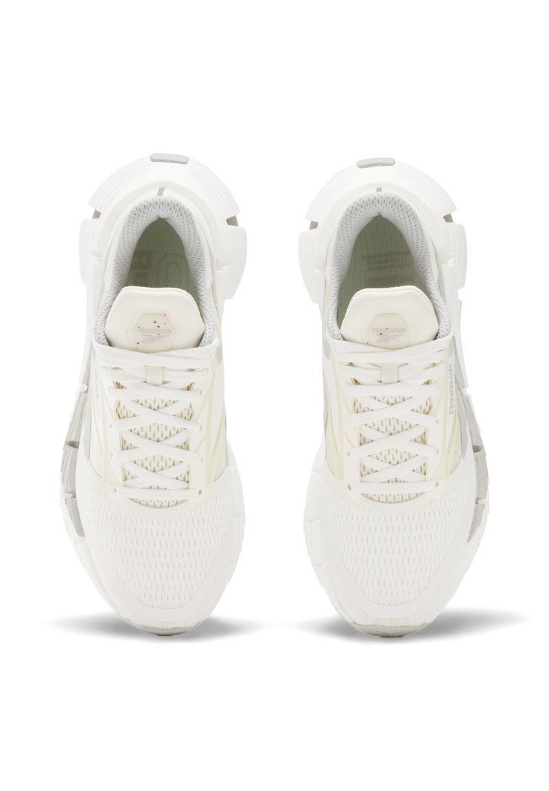 Zapatillas deportivas blancas con parte superior de malla, cordones planos, suela acolchada y sutiles acentos grises. Punta redondeada y detalles texturizados por toda la zapatilla.