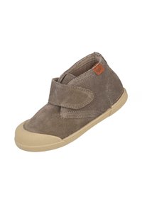 Zapato botín de ante marrón con una correa de velcro y suela de goma beige. Presenta puntera redondeada y detalles cosidos en el material superior.