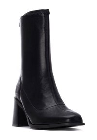 Bottine en cuir noir avec un bout pointu et un talon épais. Présente une texture lisse et des coutures minimales sur les côtés.