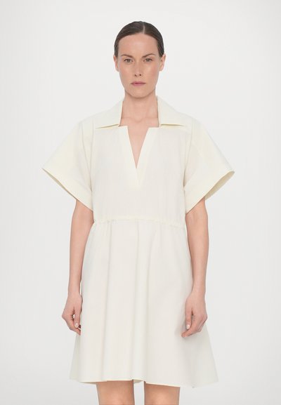 Robe crème clair avec un décolleté en V et des manches larges. Dotée d'une taille élastique et d'une jupe fluide, fabriquée à partir d'un tissu tissé lisse.