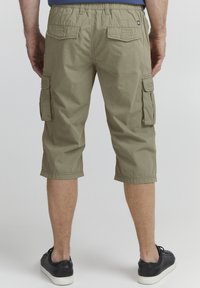 Shorts cargo en kaki avec une coupe décontractée, dotés de deux poches latérales, deux poches arrière et d'une taille élastique avec cordon de serrage. Portés avec des baskets noires.