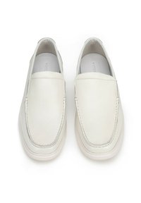 Zapatillas blancas sin cordones, hechas de cuero texturizado, con costuras contrastantes y una suela lisa y redondeada.