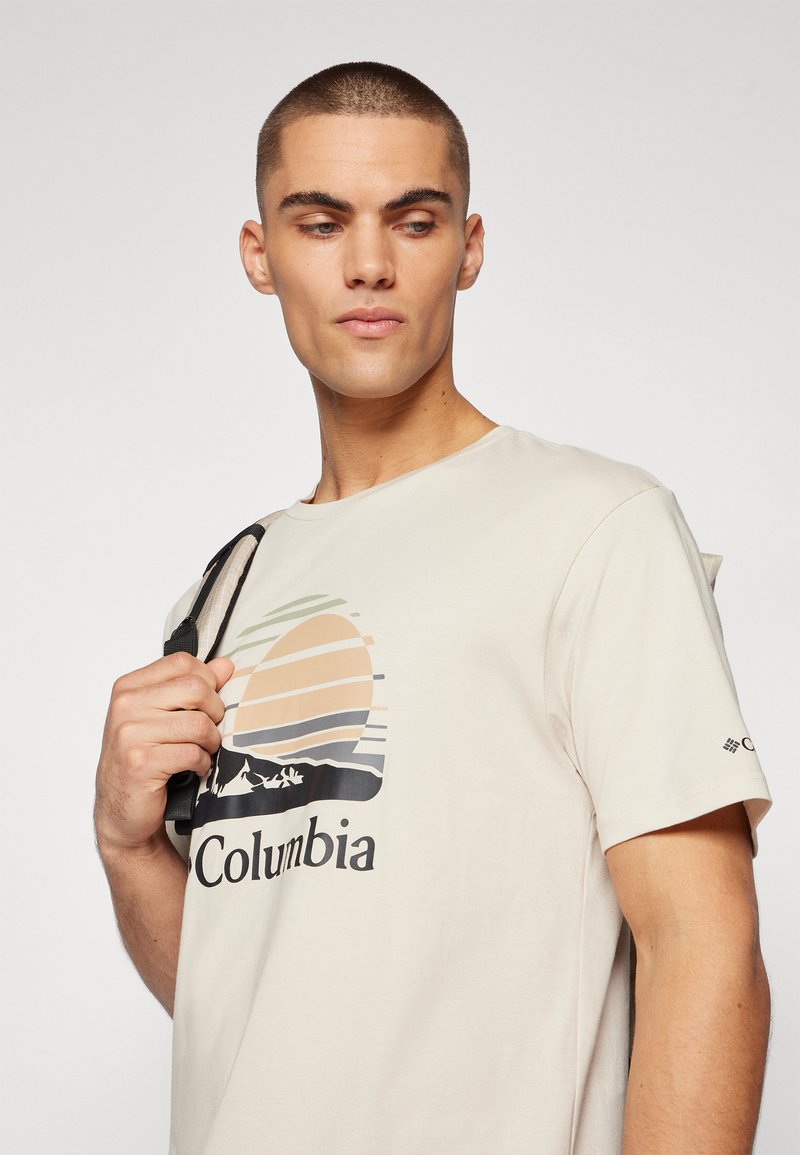 T-shirt in cotone di colore beige chiaro con una grafica di un tramonto dai colori sfumati e il testo "Columbia". Maniche corte e logo sulla manica.