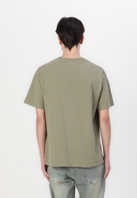 Olive green cotton t-shirt with short sleeves, crew neck, and a loose fit, paired with light blue faded jeans.