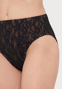Bas de bikini taille haute en dentelle noire avec motifs floraux, présentant un design en maille texturée et des bords lisses.