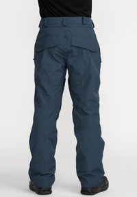 Dark blue snow pants made of water-resistant material, featuring two back pockets, reinforced knees, and adjustable waistband for a secure fit.