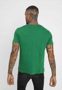 Vihreä lyhythihainen t-paita, joka on valmistettu sileästä kankaasta. Paita on pyöreäkauluksinen ja kapeamuotoinen. Takaa näkyy siisti helma ja minimalistinen muotoilu.