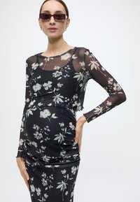 Μαύρο φόρεμα με λουλουδένιο σχέδιο και μακριά διάφανα μανίκια, με λευκά και ανοιχτό γκρι ανθάκια. Ελαφρώς πιεσμένο στη μέση για εφαρμοστή εμφάνιση.