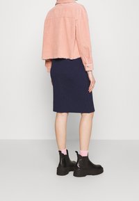 Różowa, krótkia kurtka z sztruksu, granatowa dopasowana spódnica, czarne botki na grubej podeszwie oraz różowe skarpetki. Kurtka z detalem postrzępionego brzegu.