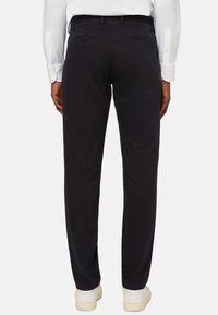 Mustia puuvillaisia housuja, joissa on kapea istuvuus, kahdella takataskulla vetoketjulla ja sileällä pinnalla, käytettynä valkoisten lenkkareiden kanssa.