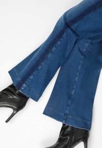 Donkerblauwe flared denim jeans met een contrasterende marineblauwe zijstreep, afgewerkt met een nette zoom. Gecombineerd met zwarte hoge enkellaarsjes.