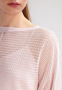 Haut en tricot rose clair avec un design en maille ouverte, doté d'un large décolleté et d'une coupe décontractée. Texture douce et léger éclat.