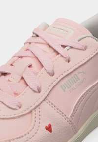Εγγύς λήψη ενός ροζ αθλητικού παπουτσιού Puma Palermo με ροζ κορδόνια, πάνελ από σουέντ και δέρμα, και μια μικρή κόκκινη καρδιά κοντά στη σόλα.