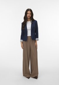 Jūras spēku žakete virs baltas blūzes, kopā ar bežām platām biksēm un brūnām zābakiem ar norādītu purngalu. Žaketei ir strīpota aproces detaļa.