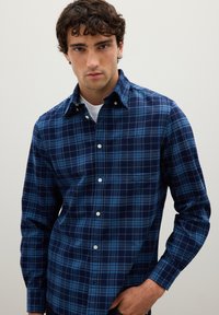 Navy and blue checkered button-up shirt with a spread collar and white buttons, featuring a chest pocket and a smooth cotton texture.