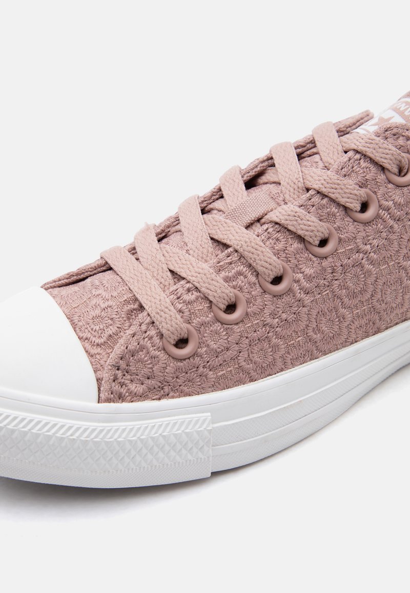 Hellrosa Sneaker aus floral strukturiertem Stoff, mit passenden Schnürsenkeln, weißer Gummikappe und weißer, gemusterter Sohle, seitlich betrachtet.