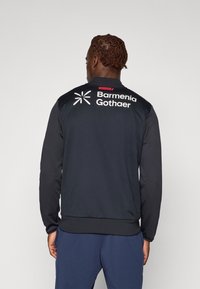 Svart sportjacka i meshmaterial, med kontrasterande ärmar och ribbade muddar. Har "Barmenia Gothaer" logotyp och "WERKSELF" etikett på baksidan.
