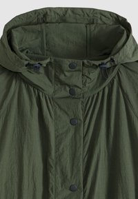 Veste légère verte avec capuche, fermeture à boutons, cordon de serrage et tissu texturé à l'aspect froissé.