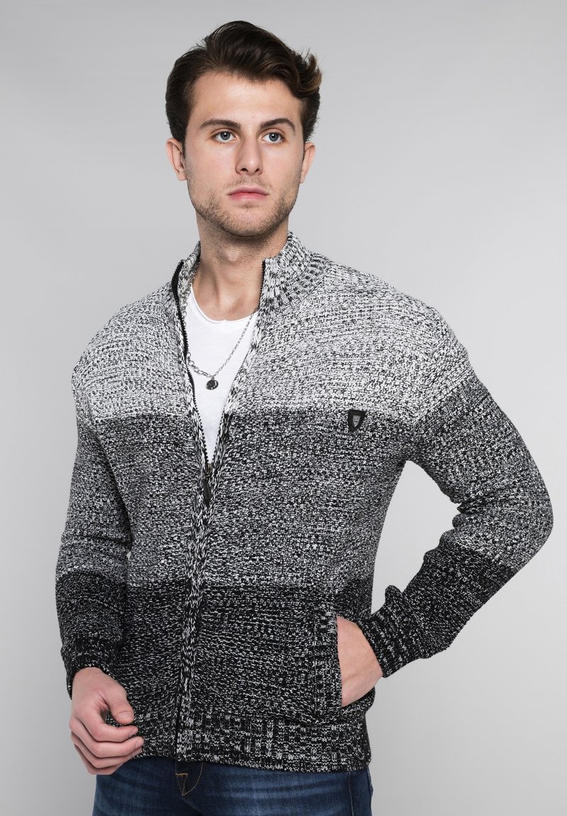 Gestrickte Zip-Up-Strickjacke in Grau und Schwarz mit einem strukturierten Muster. Verfügt über einen Stehkragen und Seitentaschen.