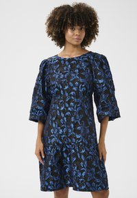Sininen brodeerattu mekko, jossa on musta pohja, puffihihat ja kerroksellinen helma, jossa on floral kuvioita ympäriinsä.