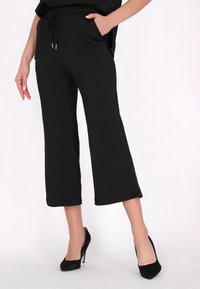 Svarta cropped byxor med ett strukturerat mönster, med en elastisk midja och sidofickor, tillsammans med svarta högklackade skor.