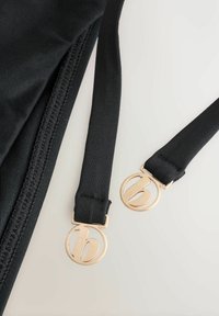 Zwarte stoffen banden met goudkleurige cirkelvormige sluiting met een gestileerd kleine letter "b" ontwerp; gladde textuur, stevige constructie.