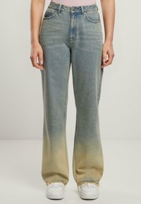 Jeans de tiro alto en un tono azul claro con un degradado desvanecido a amarillo pálido en el dobladillo. Con bordes deshilachados y un diseño de pierna recta.
