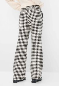 Brede broek in een zwart-wit houndstoothpatroon, met een hoge tailleband en zijzakken. De stof lijkt gestructureerd.