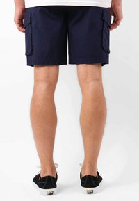 Shorts cargo bleu marine en coton, avec poches latérales, coupe droite et un ourlet juste au-dessus du genou, associés à des baskets noires.