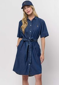 Rifľové šaty košeľového strihu v tmavomodrej farbe s krátkymi rukávmi, zapínaním na gombíky a zaväzovaním v páse. Dopĺňa ich zodpovedajúca tmavomodrá čiapka s logom.