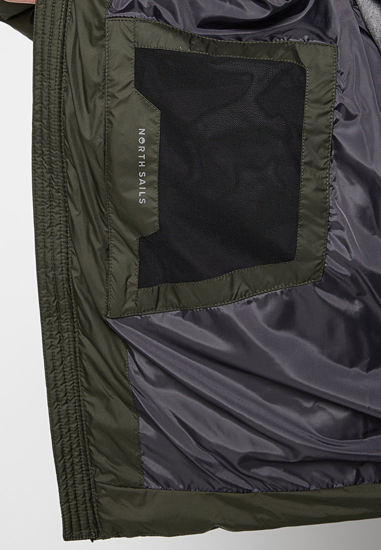 Interno della giacca verde oliva con una tasca in rete e tessuto liscio con fodera grigia. Logo "NORTH SAILS" stampato sulla tasca.