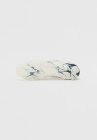 Zapato deportivo con una suela blanca, texturizada y curvada que presenta tacos translúcidos. La parte superior muestra un diseño en azul y gris con patrones florales.