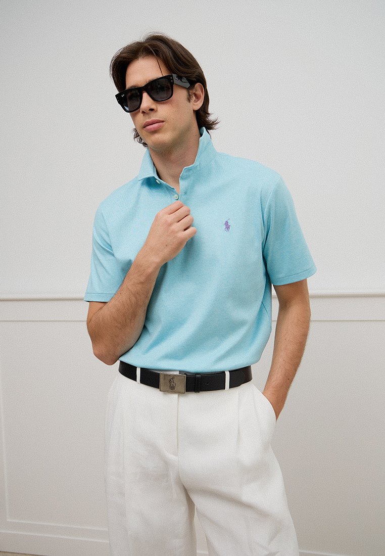 Jasnoniebieska koszulka polo z kołnierzykiem, z małym purpurowym logo. W zestawie z białymi spodniami i czarnym paskiem z metalową klamrą.
