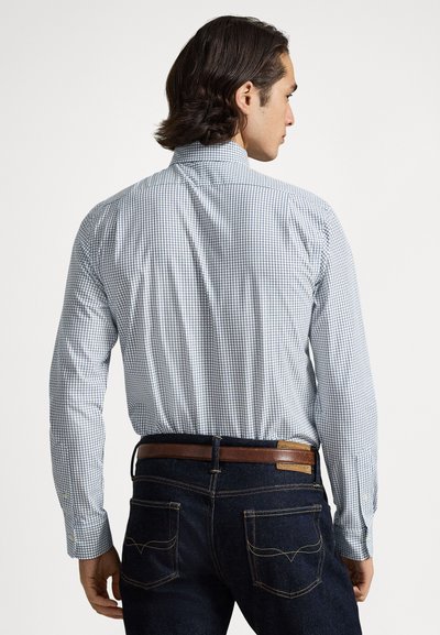 Καρό πουκάμισο, μπλε και λευκό μοτίβο, μακριά μανίκια, γιακάς με κουμπιά. Φορεμένο με σκούρο τζιν και καφέ ζώνη, εμφανίζοντας την πίσω όψη.