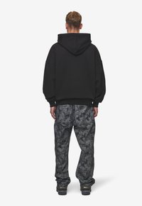 Hanorac negru oversized cu glugă reglabilă, asociat cu pantaloni gri cu un model, având o croială lejeră și un design subtil cu stropi.