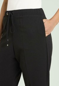 Pantalones jogger negros con cintura ajustable mediante cordón, bolsillos laterales y una tela suave y elástica con un ajuste relajado.