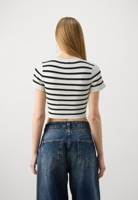 Kuttet t-skjorte i hvitt med svarte horisontale striper, korte ermer og tettsittende passform, parret med høyt liv blå denim-jeans.