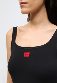 Μαύρο αμάνικο τοπ με στρογγυλή λαιμόκοψη, με κόκκινη ορθογώνια ετικέτα στο κέντρο με την επιγραφή "HUGO". Λείο ύφασμα.