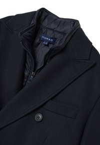 Cappotto in misto lana blu navy con fodera interna trapuntata, colletto a revers, chiusura con un solo bottone e tasca sul petto.