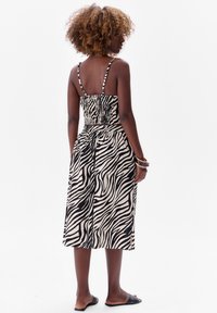 Zwart-witte jurk met zebra-strepen, een strakke, gerimpelde bovenkant, verstelbare bandjes en een vloeiende rok die tot de knie komt.