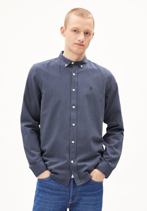Navy striped button-up shirt with long sleeves and a collar; features white buttons and a small logo on the chest. Worn with blue jeans.