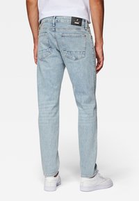 Jeans de mezclilla de color azul claro con pierna recta, bolsillos traseros visibles y una etiqueta de marca negra; usados con zapatillas blancas.