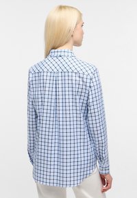 Light blue plaid shirt with long sleeves, a pointed collar, and a curved hem. Made from smooth fabric with a button closure at the cuffs.